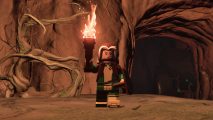 Lego Rogue is standing in front of the Lego Fortnite knotroot inside of a cave. She is holding a torch to light the way.